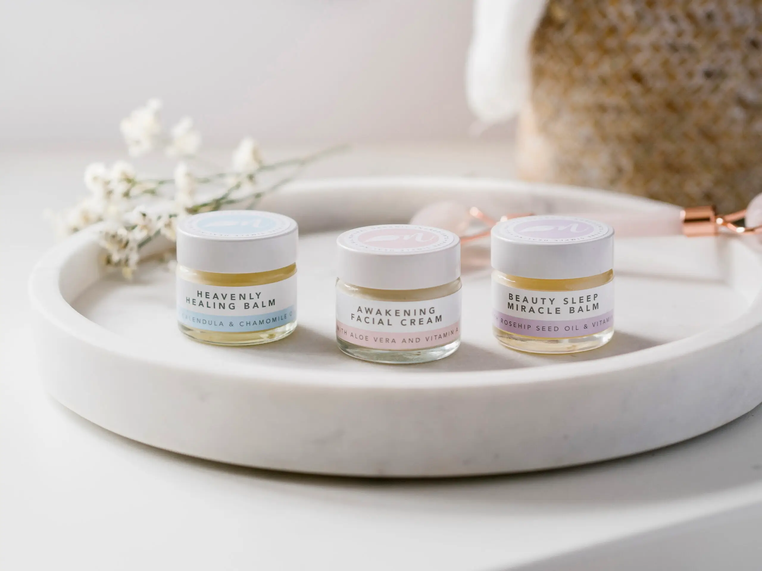 A picture of Noubalm Heavenly Healing Balm, Noubalm Awakening Facial Cream, and Noubalm Beauty Sleep Miracle Balm on a white marble plate